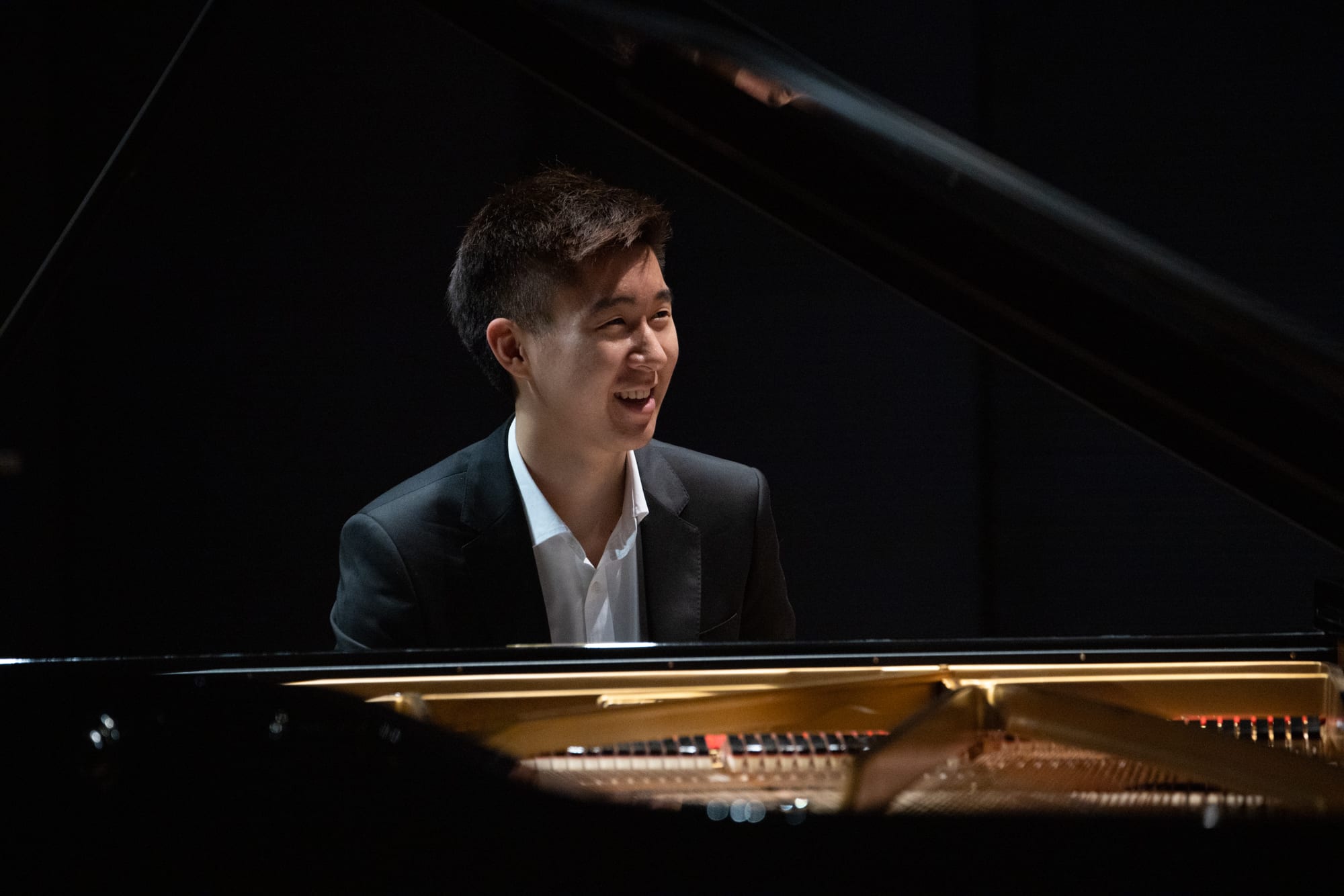 Samuel Choi smiling while seated at a grand piano